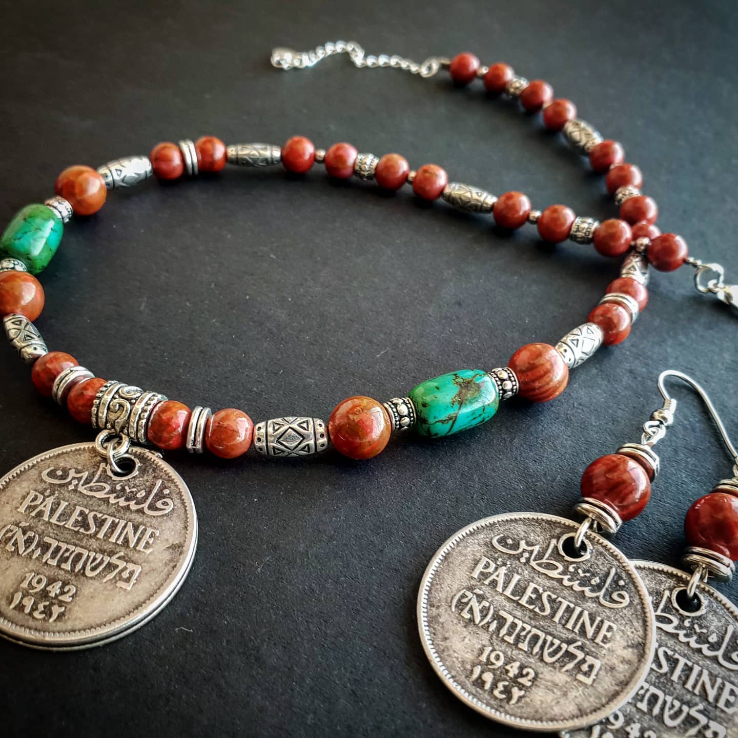 Necklace with orange and green beads and vintage Palestinian coins on a dark surface