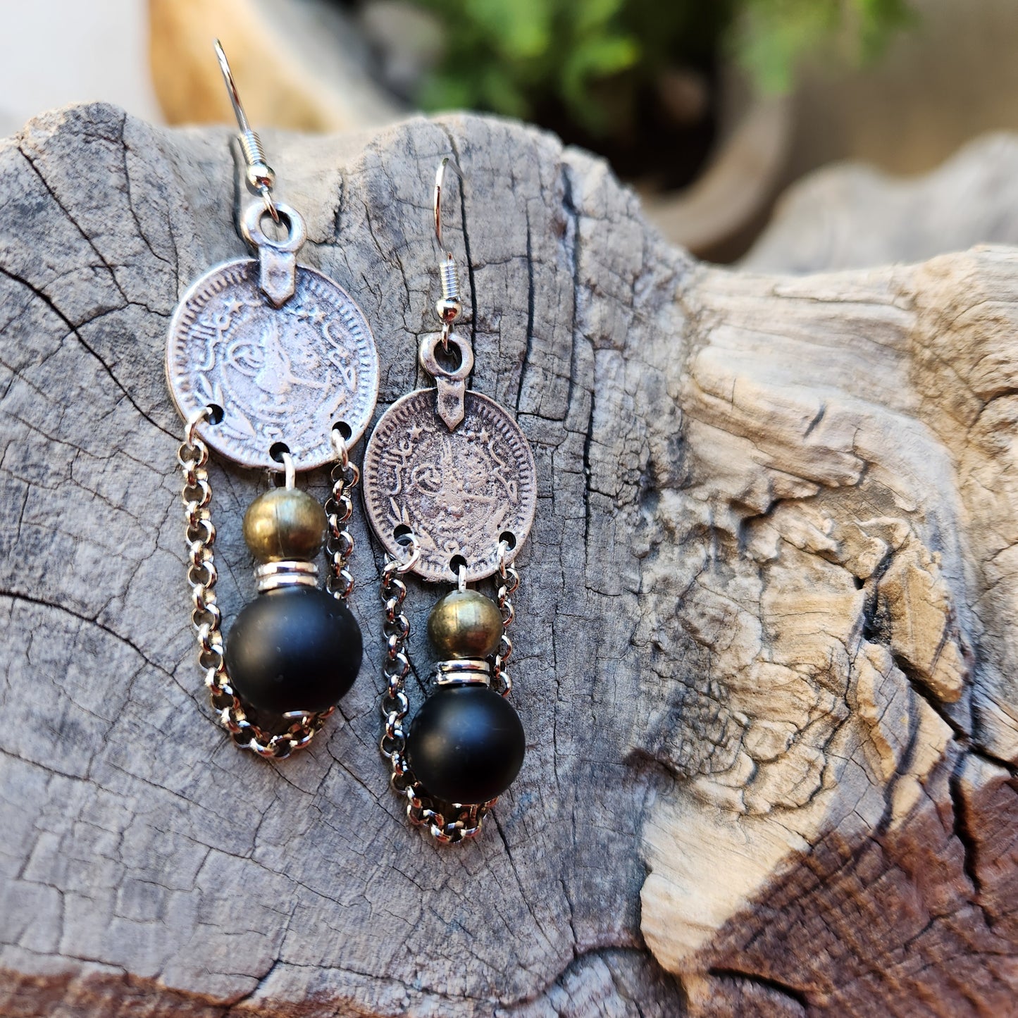 Pair of earrings with coin and black bead design on a wooden surface