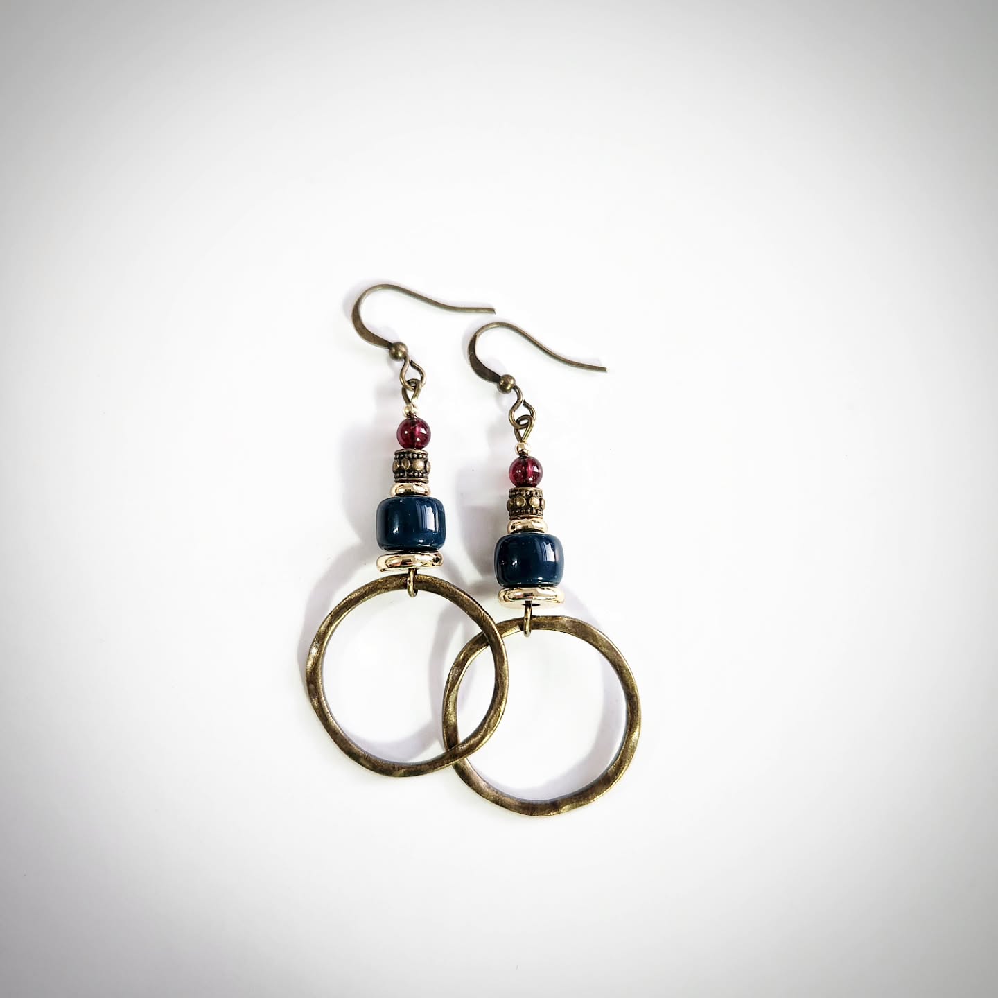 Pair of bronze earrings with circular designs with red and blue beads on a white background