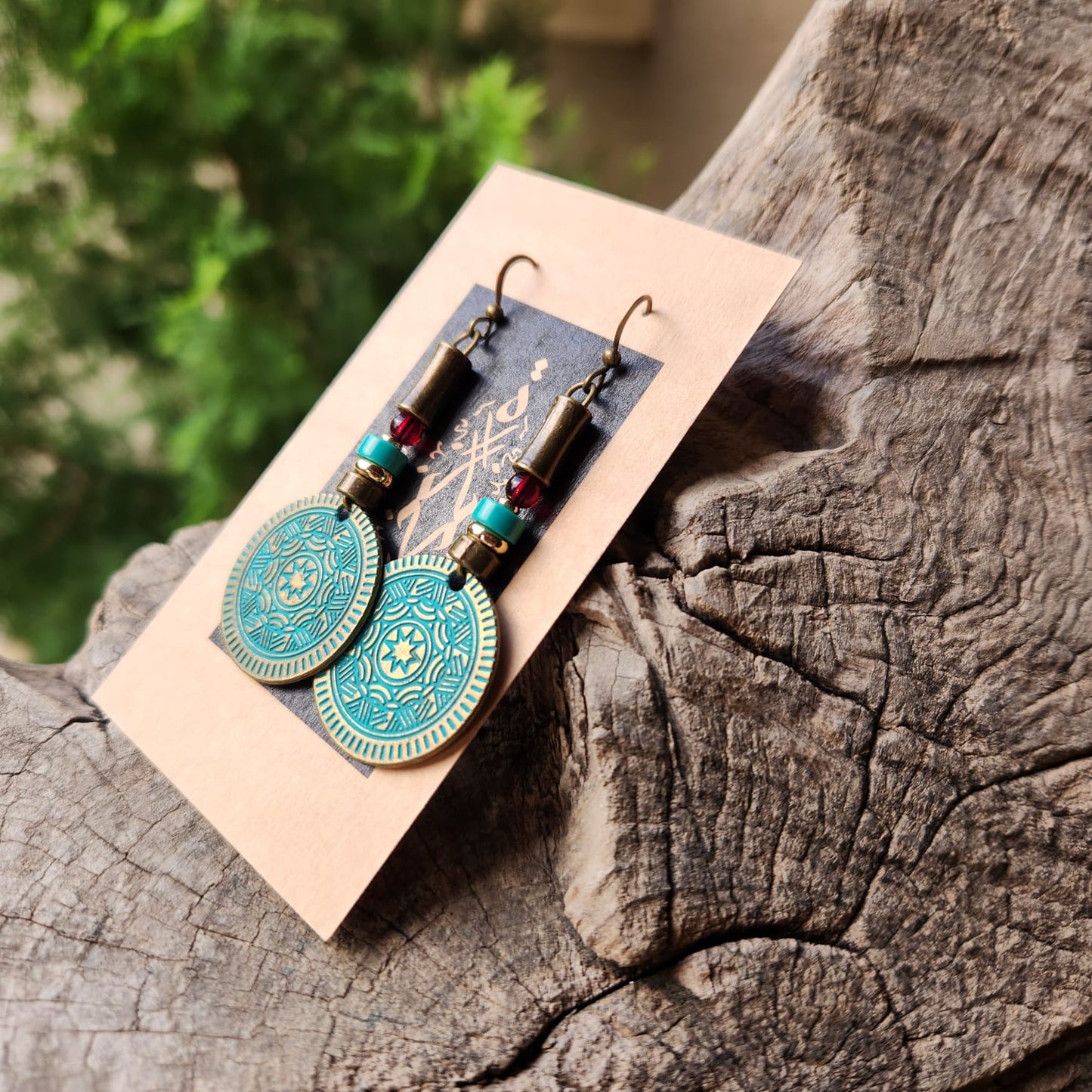Pair of bronze and turquoise earrings on a card, placed on a wooden surface with a blurred green background