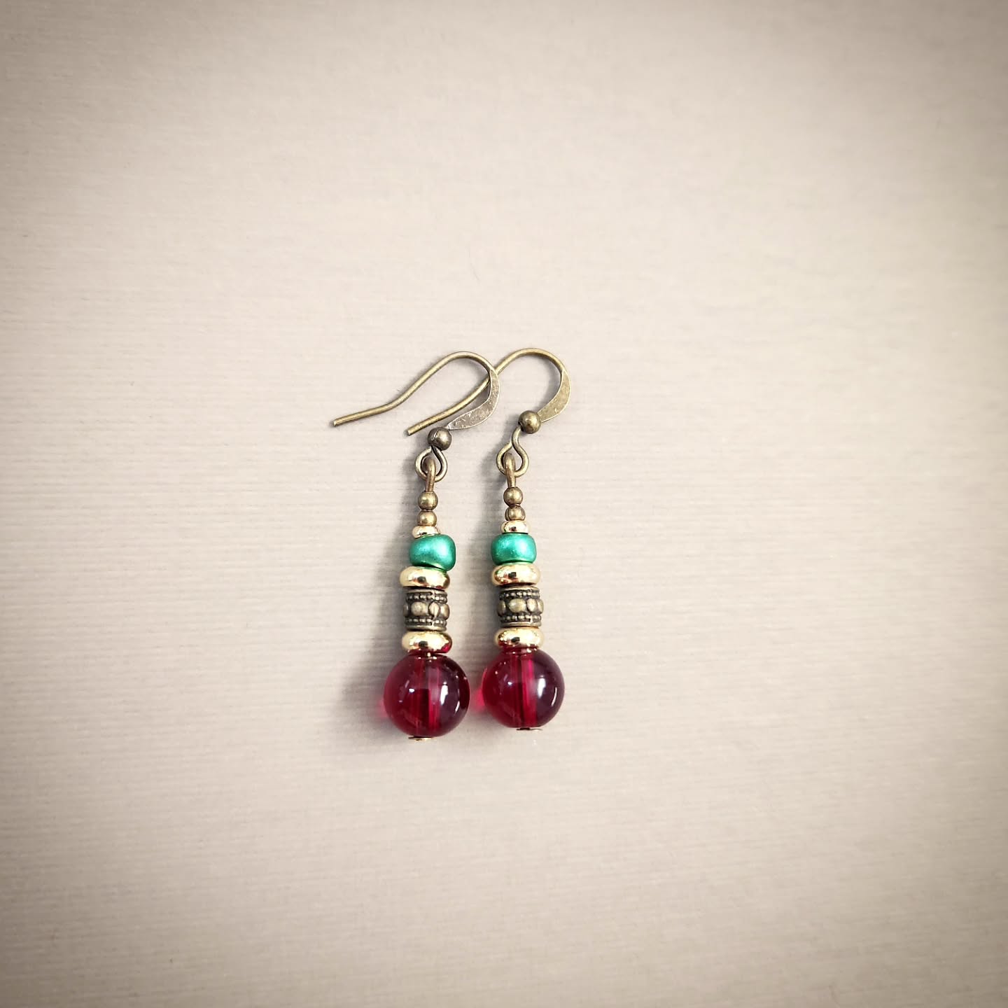 Pair of earrings with red, gold and turquoise beads on a beige background
