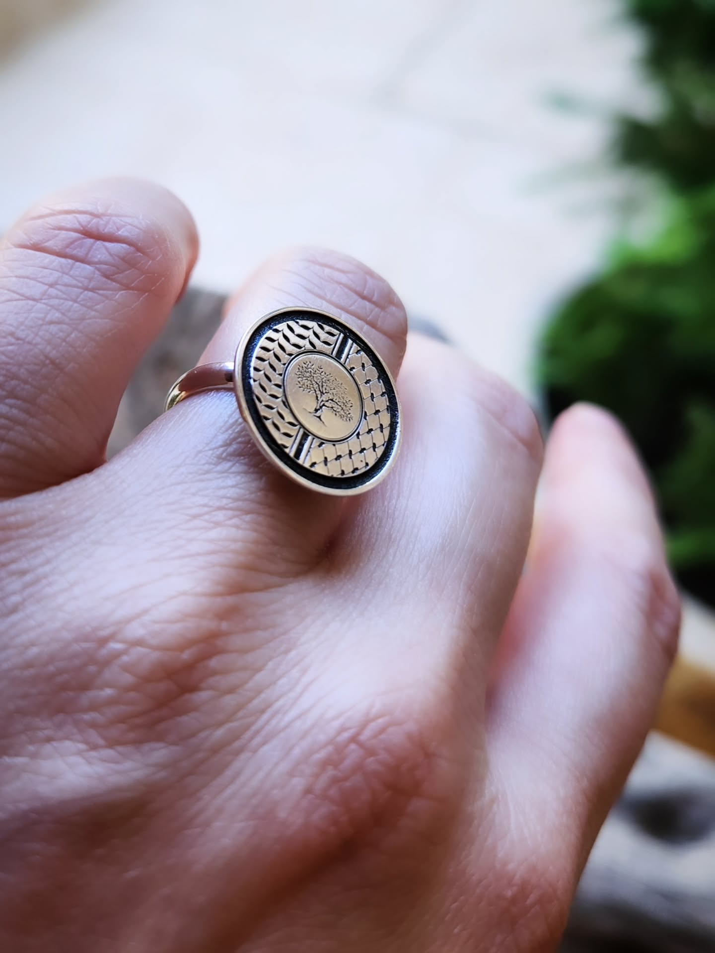 Close-up of a hand wearing a silver ring with a tree design on a blurred background