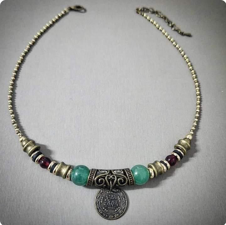 Necklace with gold and bronze beads and a coin pendant on a gray background