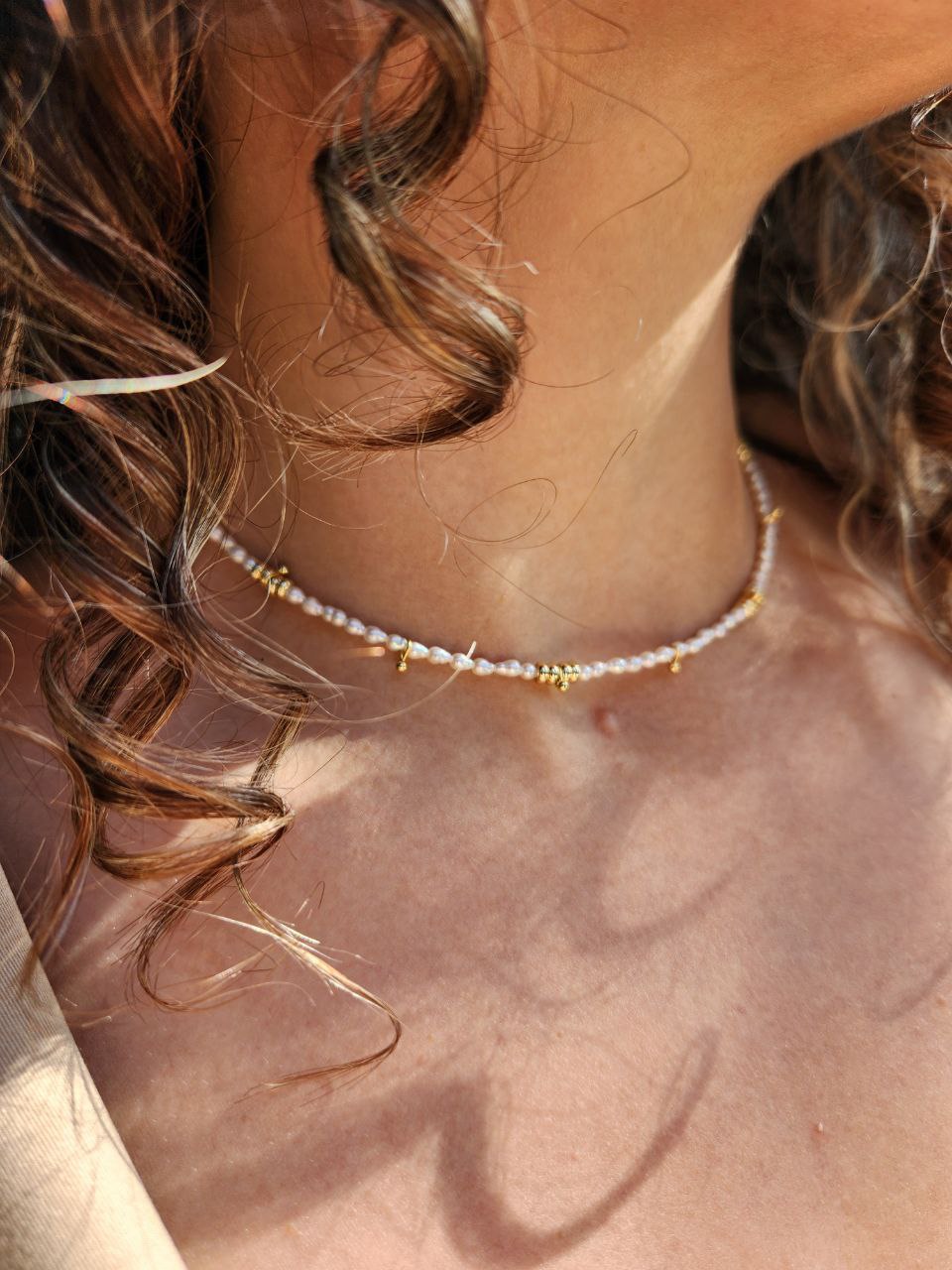 Close-up of a person wearing a necklace with pearl beads and gold accents on a light gray background