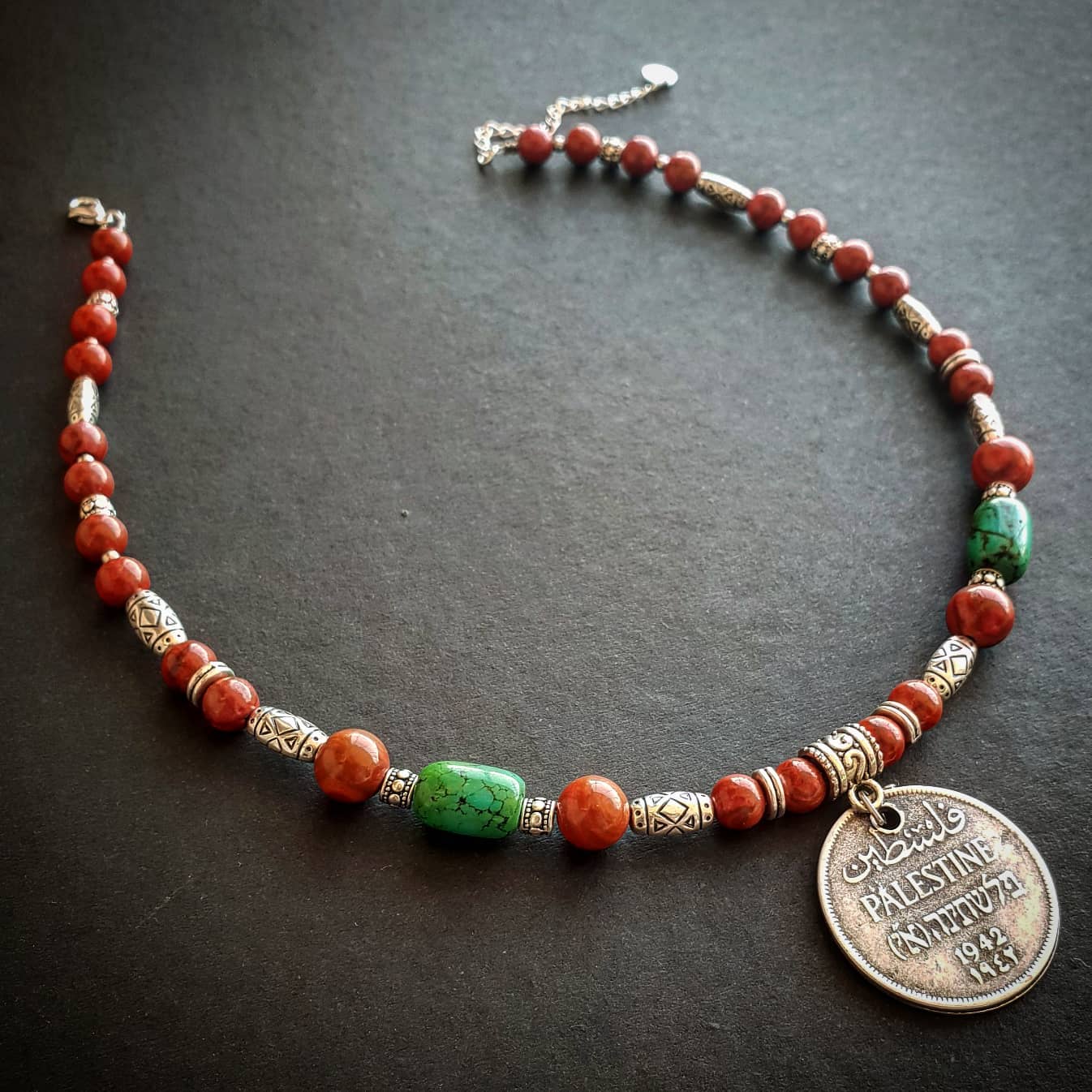 Necklace with orange and green beads and vintage Palestinian coins on a dark surface