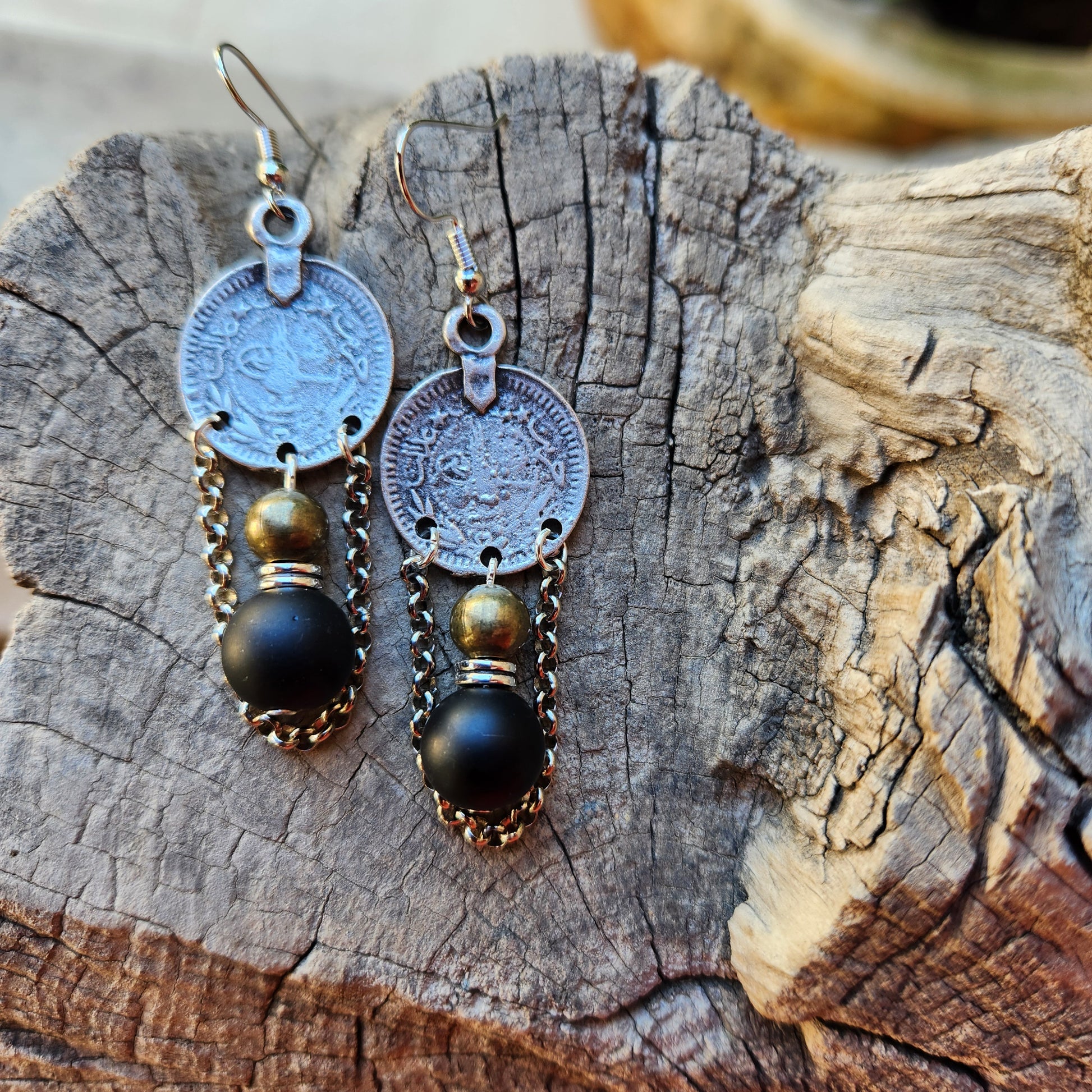 Pair of earrings with coin and black bead design on a wooden surface