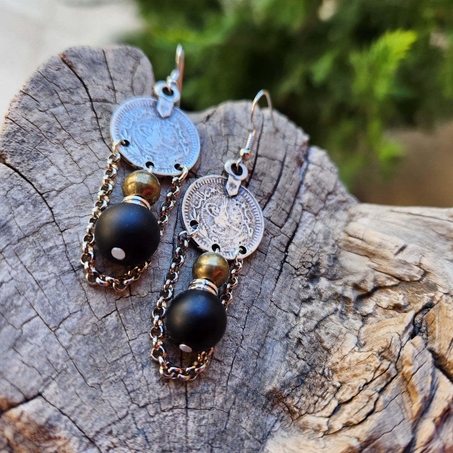 Pair of earrings with coin and black bead design on a wooden surface
