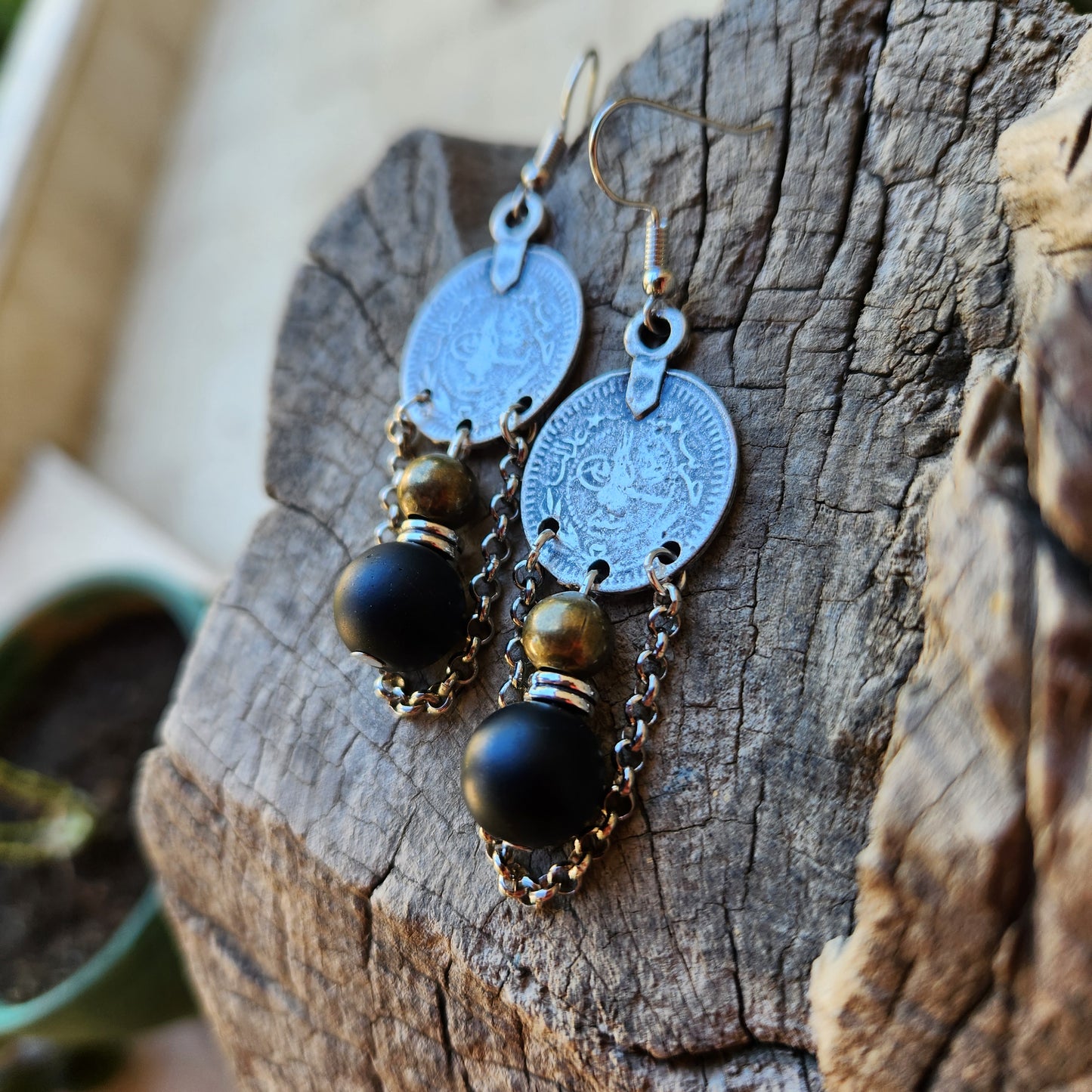 Pair of earrings with coin and black bead design on a wooden surface