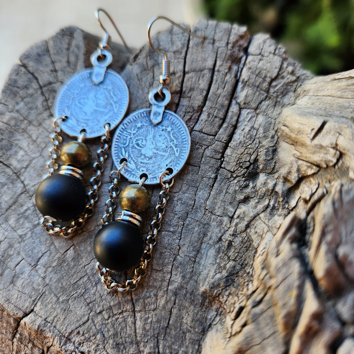 Pair of earrings with coin and black bead design on a wooden surface