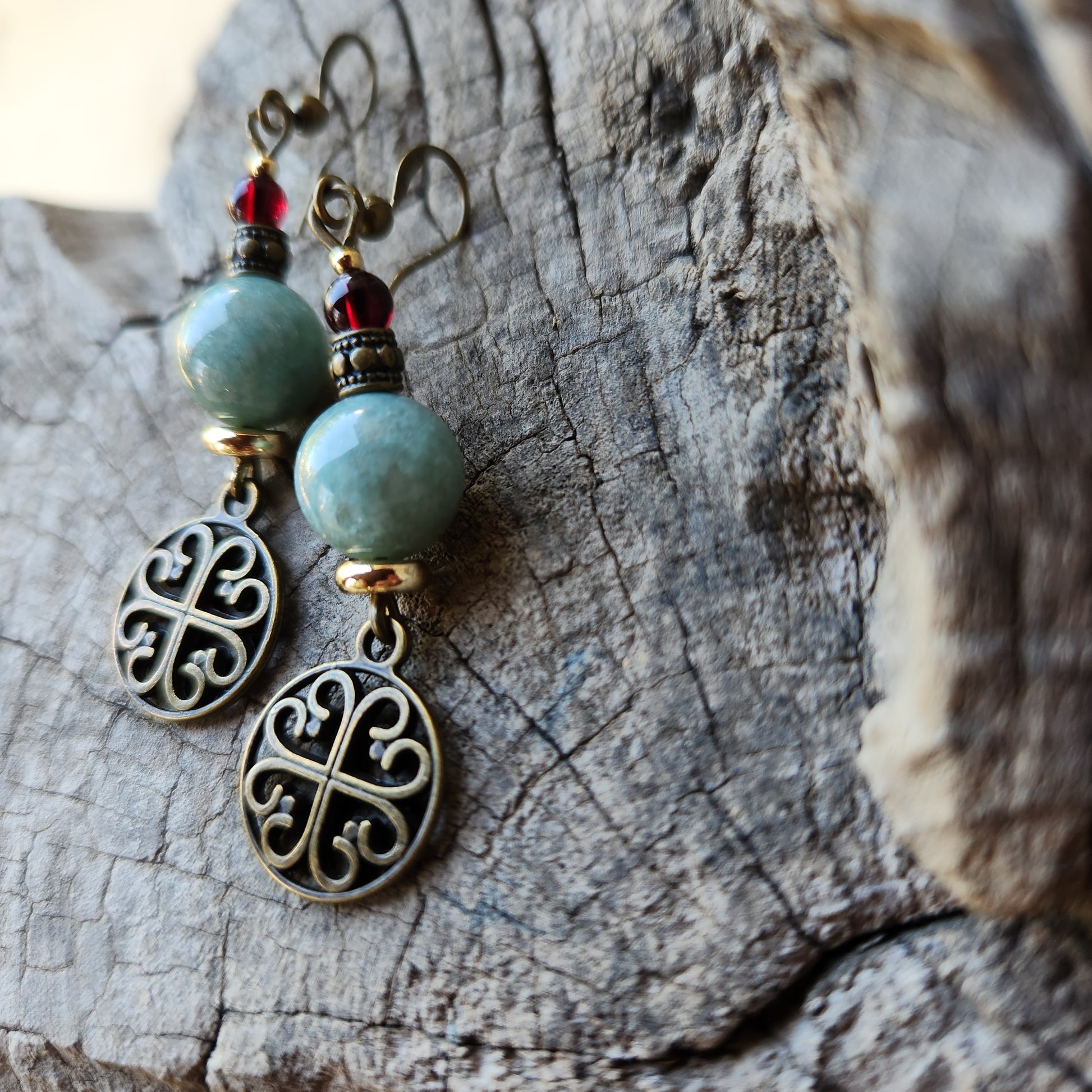 Pair of earrings with turquoise beads and bronze filigree designs on a wooden surface.