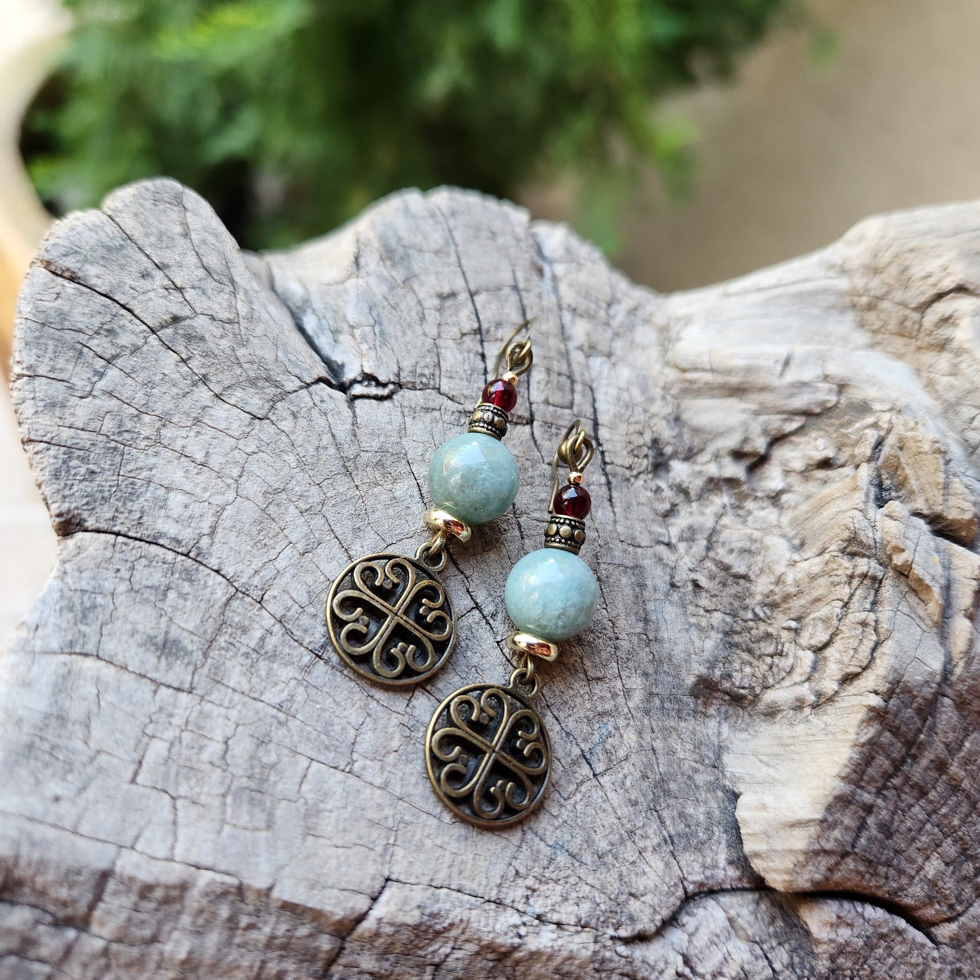 Pair of earrings with turquoise beads and bronze filigree designs on a wooden surface.