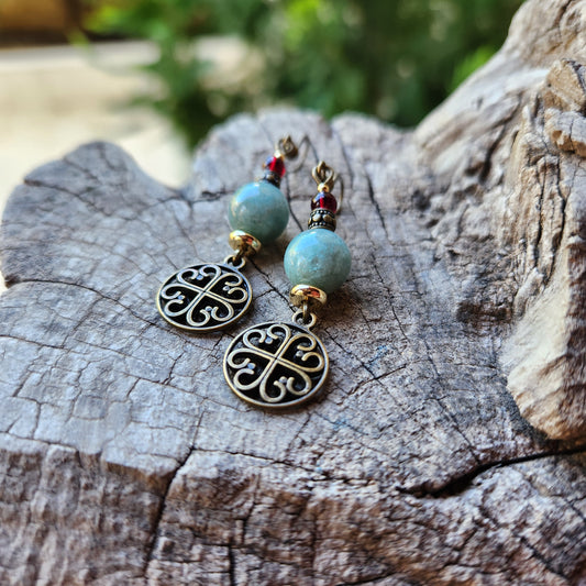 Pair of earrings with turquoise beads and bronze filigree designs on a wooden surface.