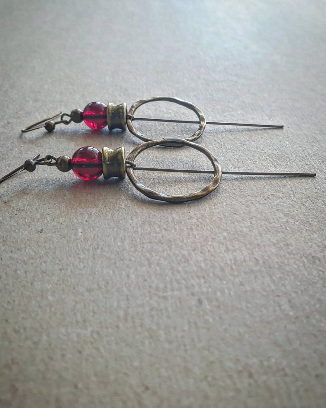 Pair of earrings with circular designs and red beads on a gray background