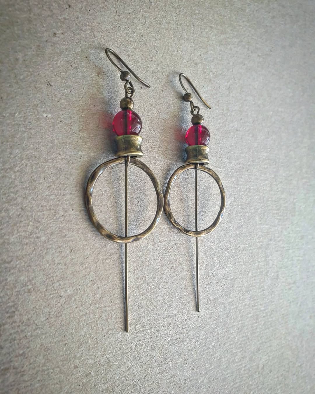 Pair of earrings with circular designs and red beads on a gray background