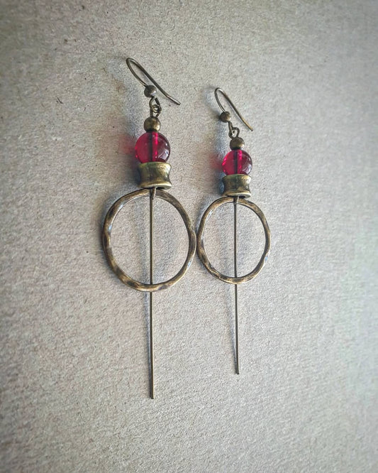 Pair of earrings with circular designs and red beads on a gray background