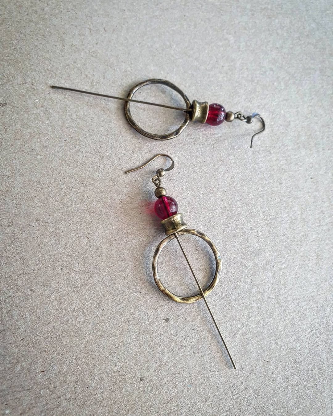 Pair of earrings with circular designs and red beads on a gray background