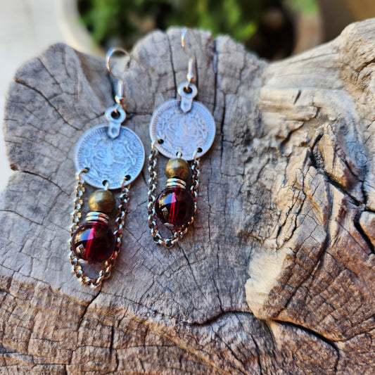 Pair of earrings with circular charms and red gemstones on a wooden surface