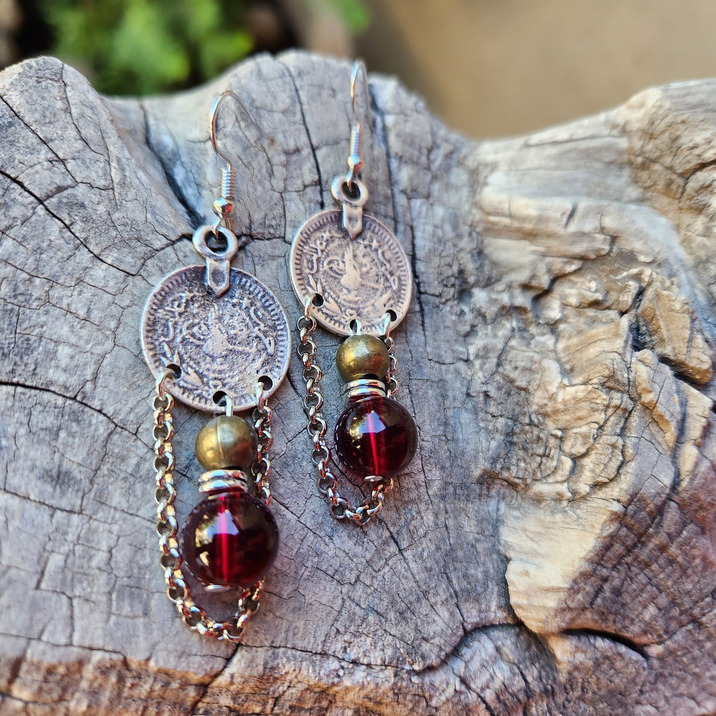 
Pair of earrings with circular charms and red gemstones on a wooden surface