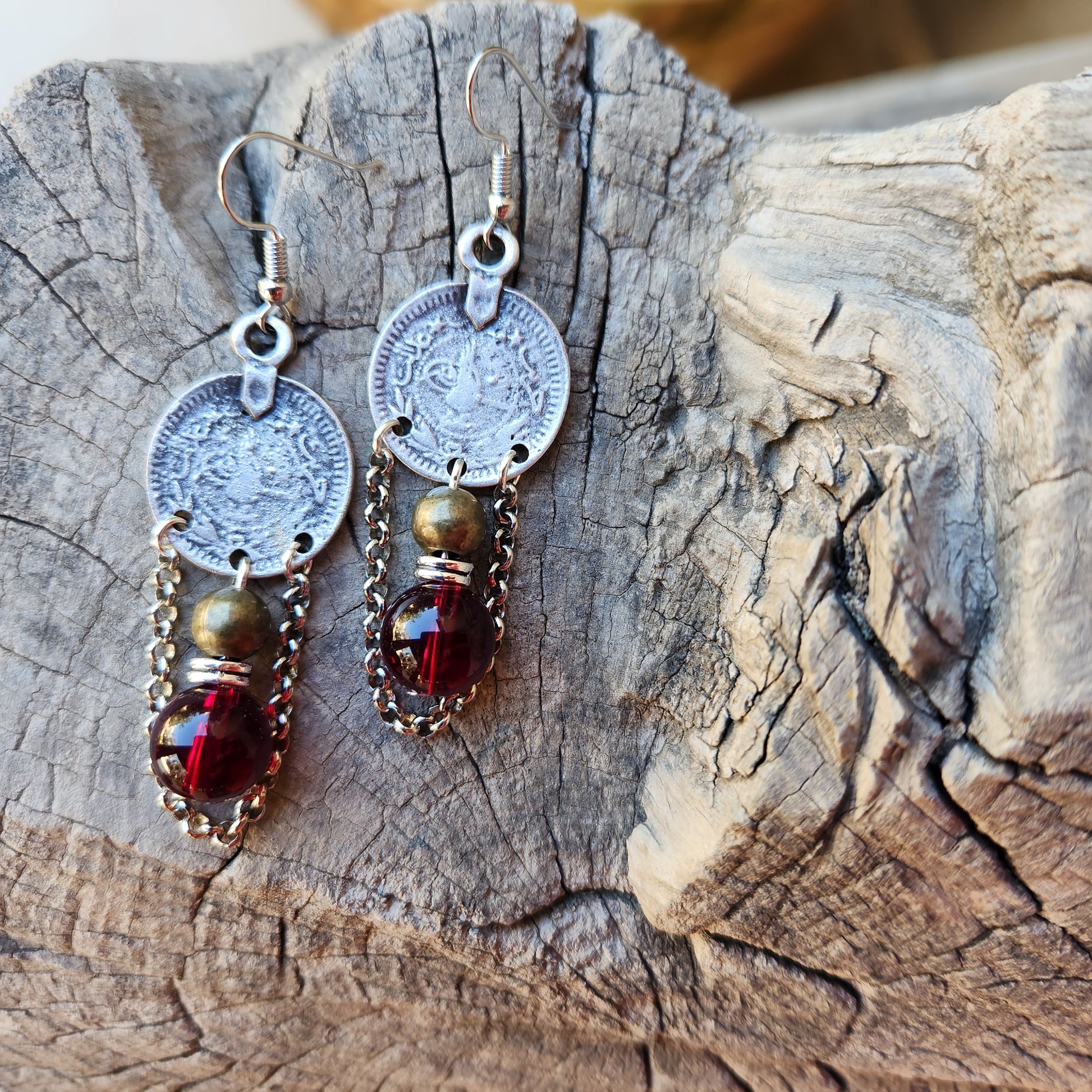 
Pair of earrings with circular charms and red gemstones on a wooden surface