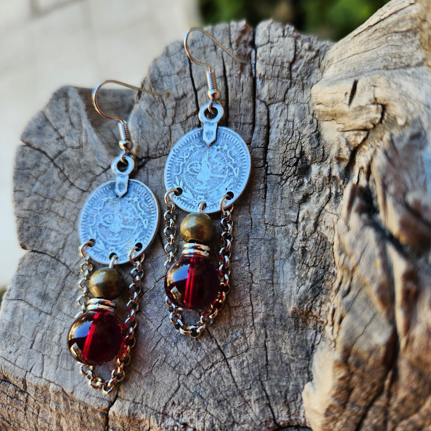 
Pair of earrings with circular charms and red gemstones on a wooden surface