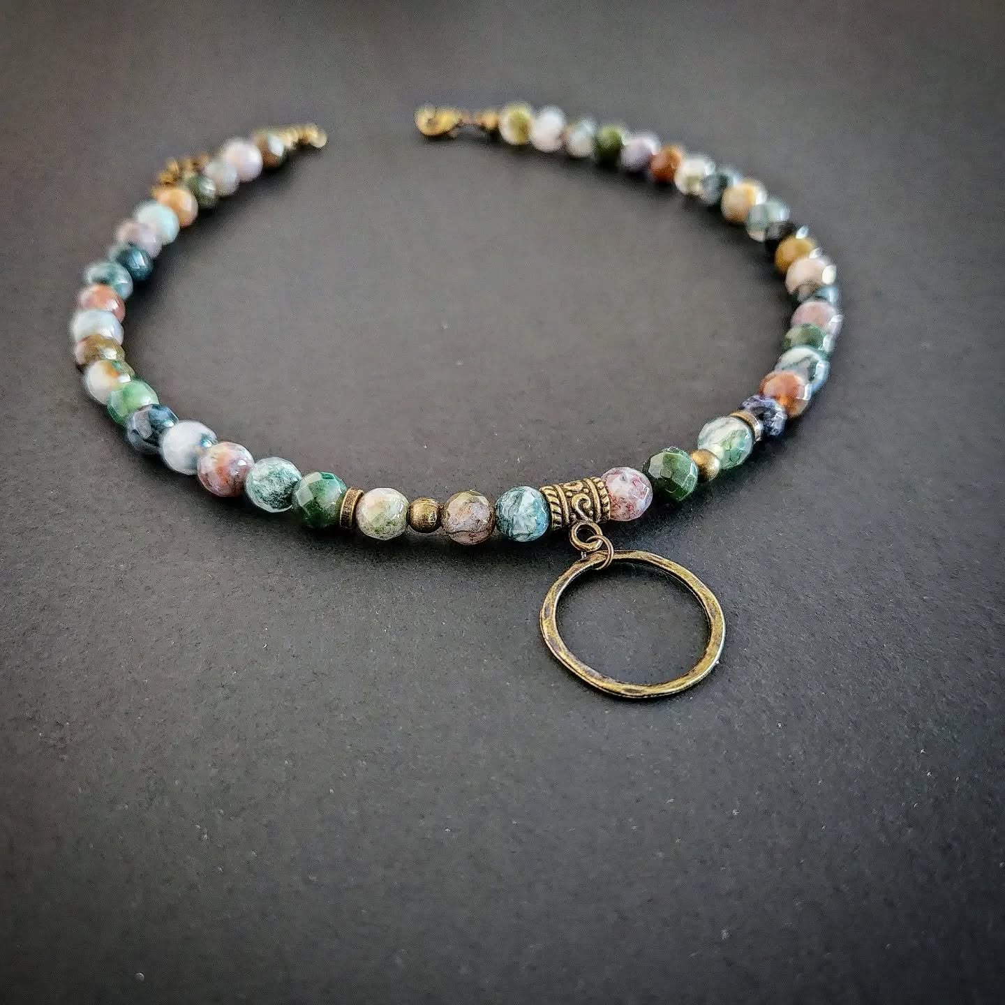 Necklace with bronze and multicolored beads and a circular pendant on a dark background