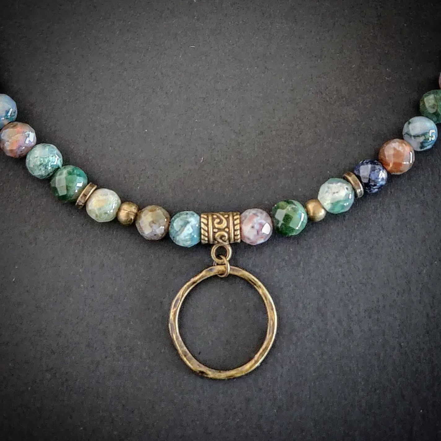 Necklace with bronze and multicolored beads and a circular pendant on a dark background