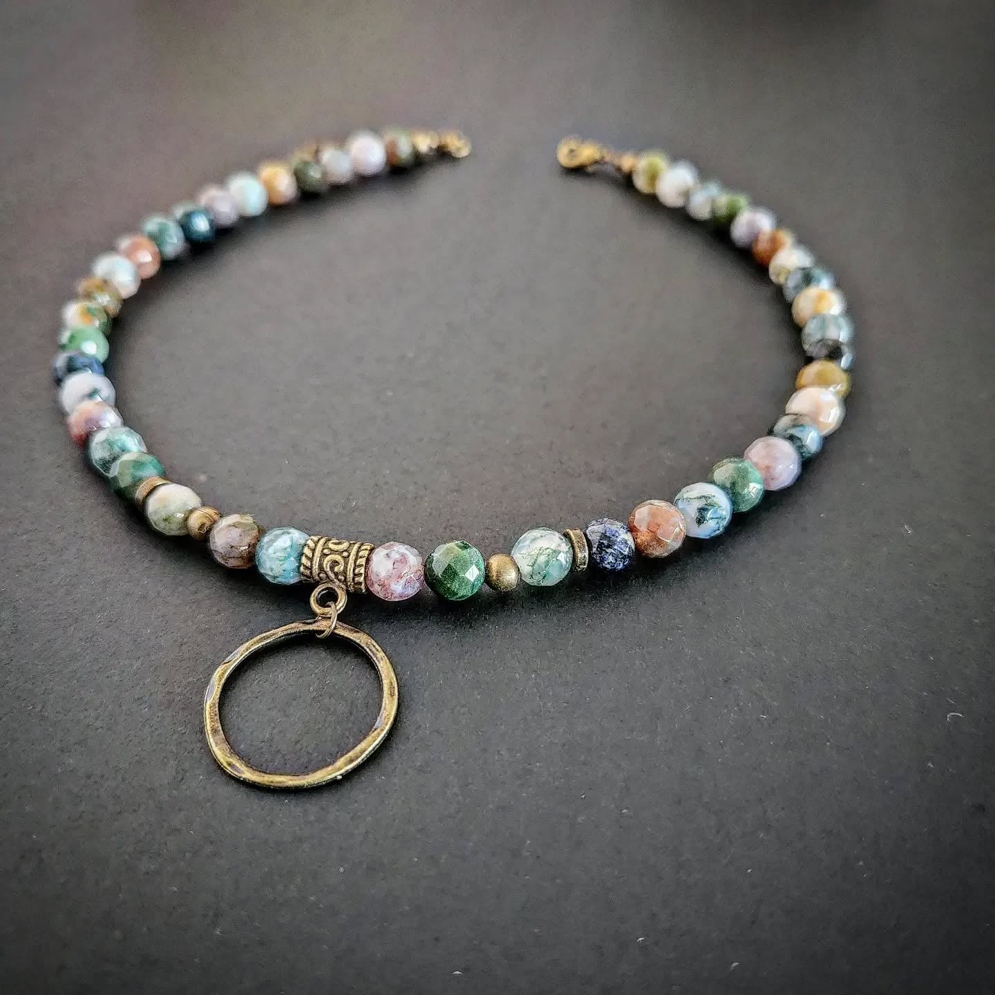 Necklace with bronze and multicolored beads and a circular pendant on a dark background