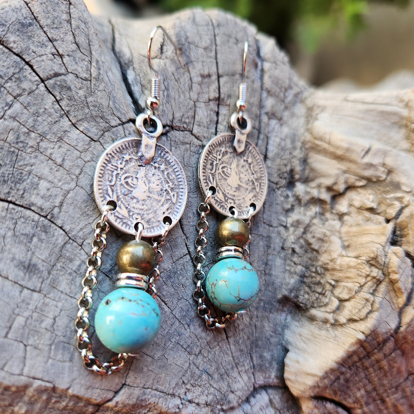 Pair of earrings with coins and turquoise stones on a wooden surface