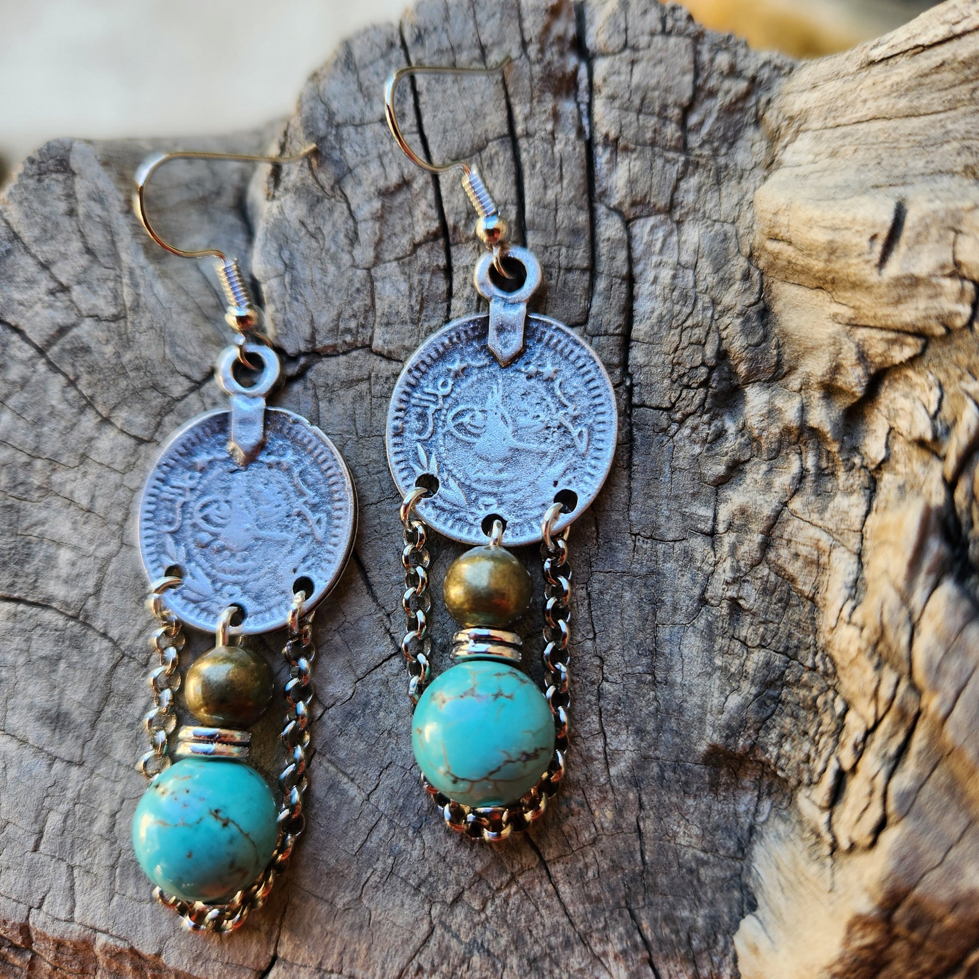 Pair of earrings with coins and turquoise stones on a wooden surface