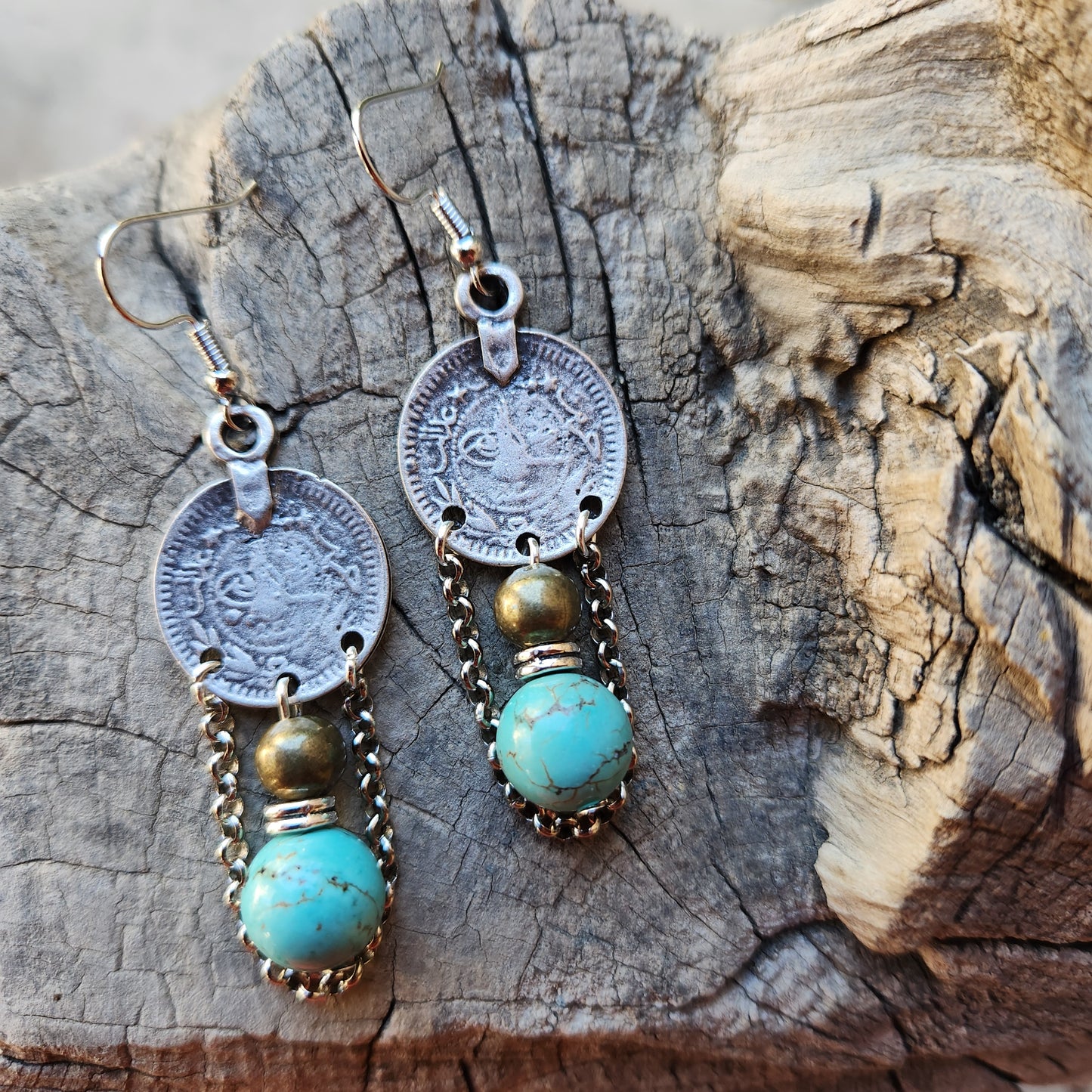 Pair of earrings with coins and turquoise stones on a wooden surface