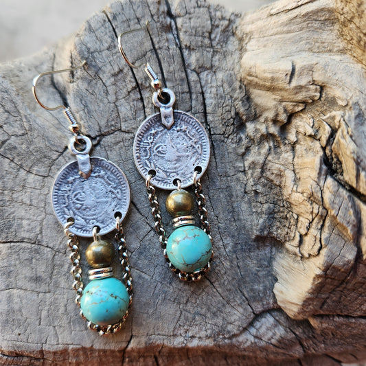 Pair of earrings with coins and turquoise stones on a wooden surface