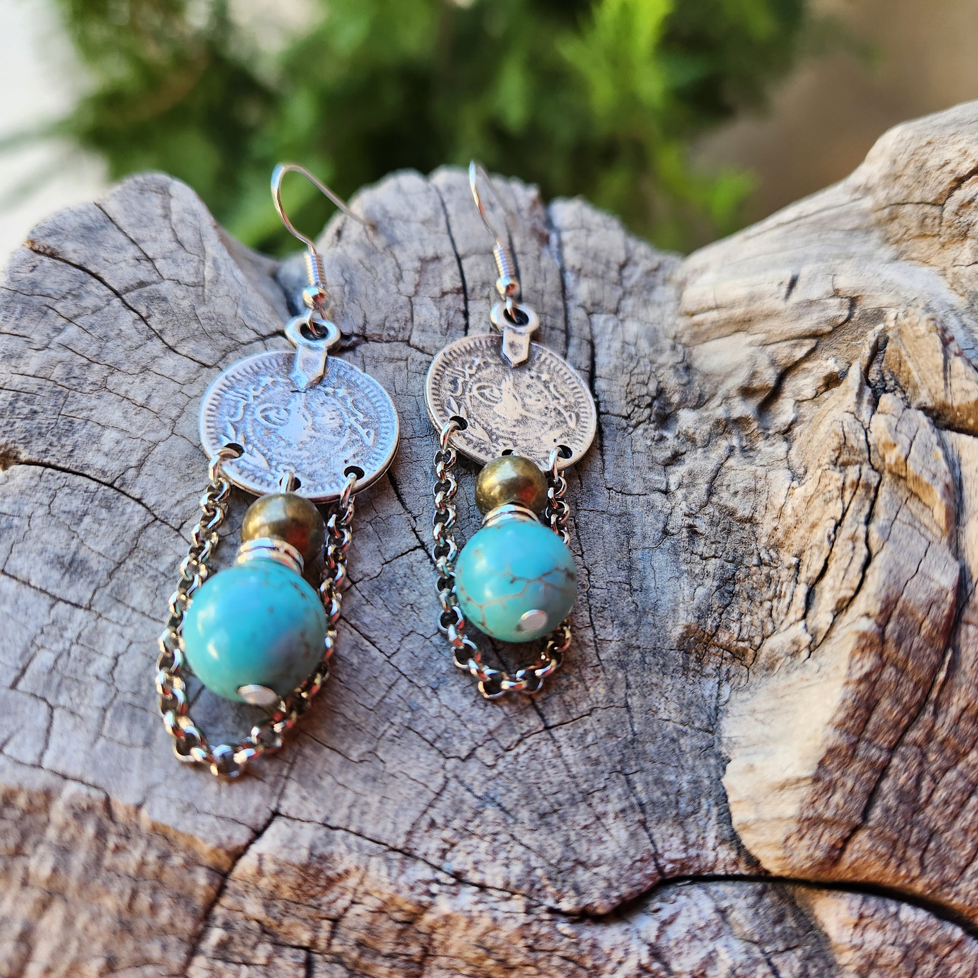 Pair of earrings with coins and turquoise stones on a wooden surface