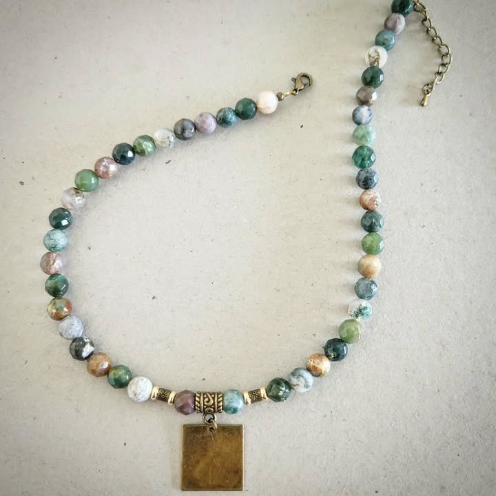 Necklace with bronze and multicolored beads and a rectangular pendant on a light gray background