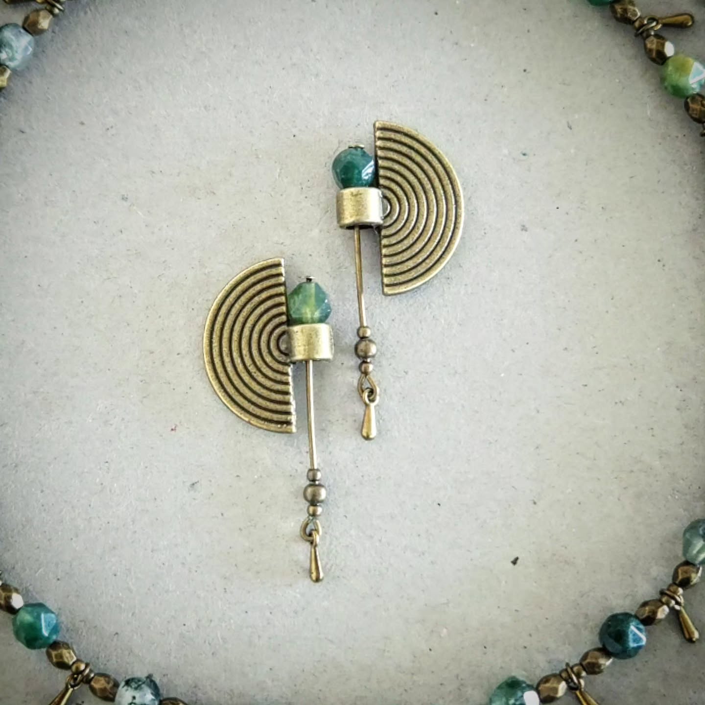 Bronze and green beaded earrings on a textured beige background