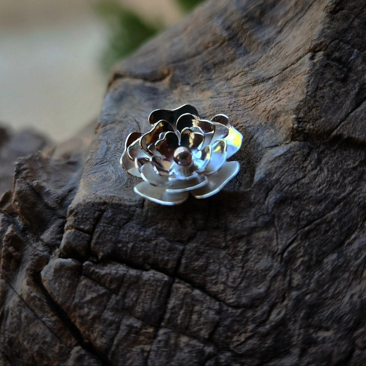 Silver flower-shaped jewelry piece on a textured wooden surface