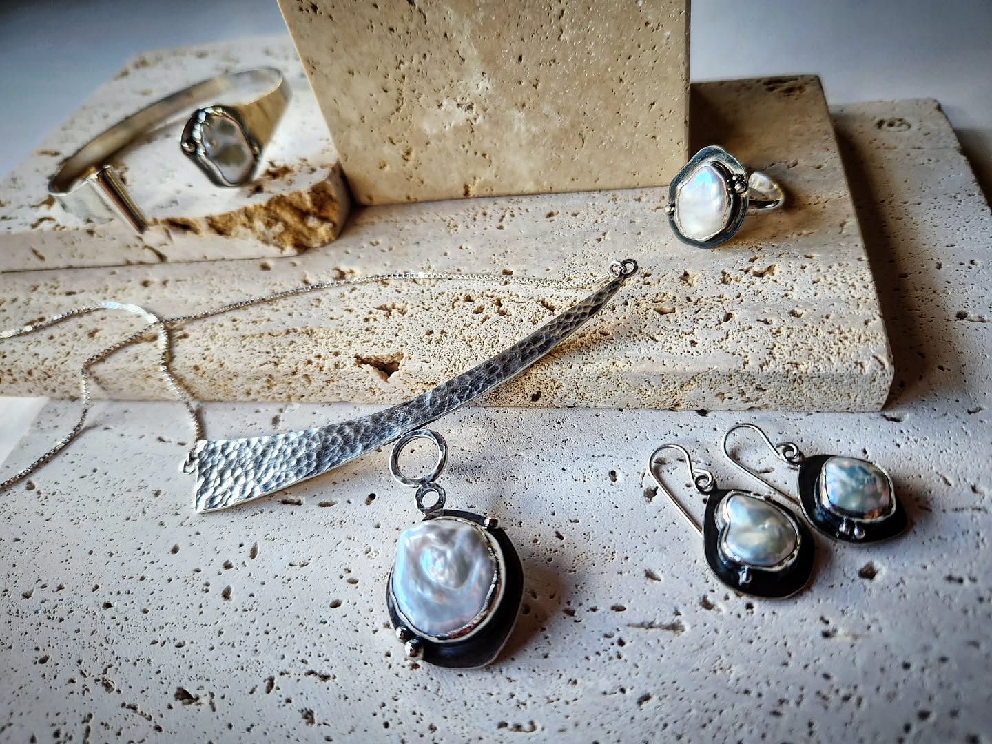 Silver jewelry set with pearls on a textured surface