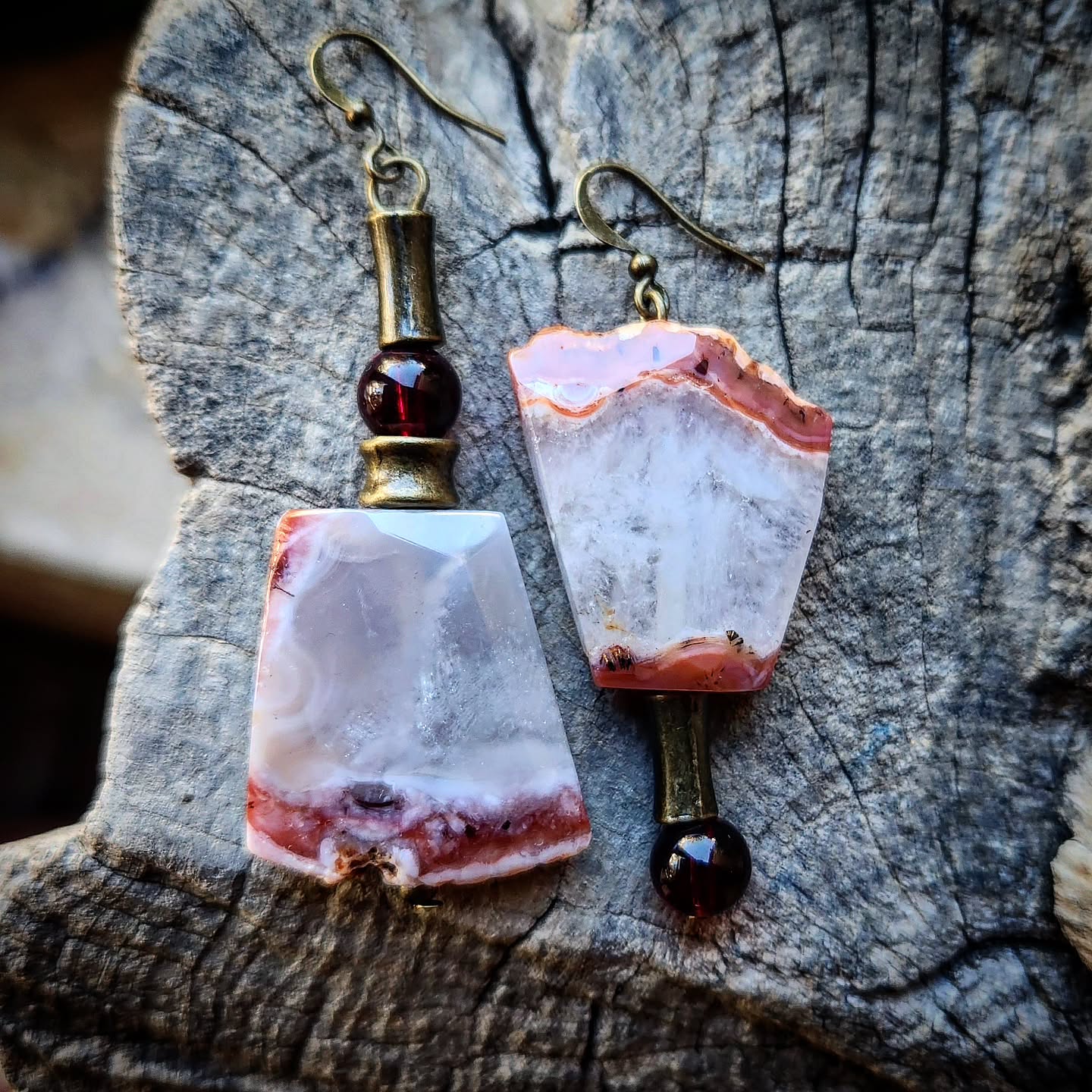 Pair of earrings with agate-like stones and garnet stones on a wooden surface