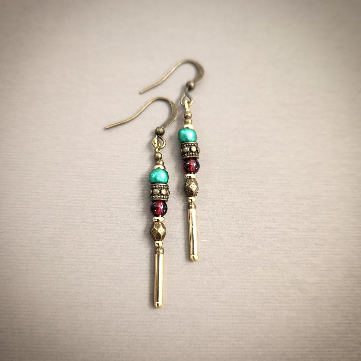 Pair of beaded earrings with gold and colorful beads on a beige background