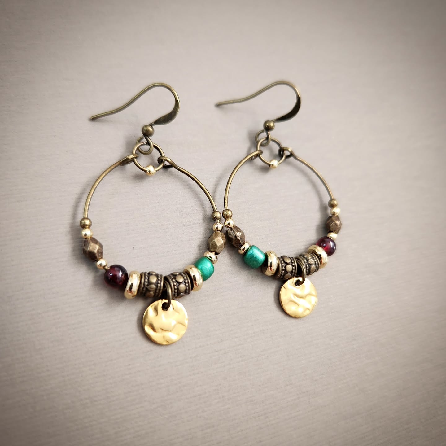 Pair of hoop earrings with beads and gold accents on a gray background
