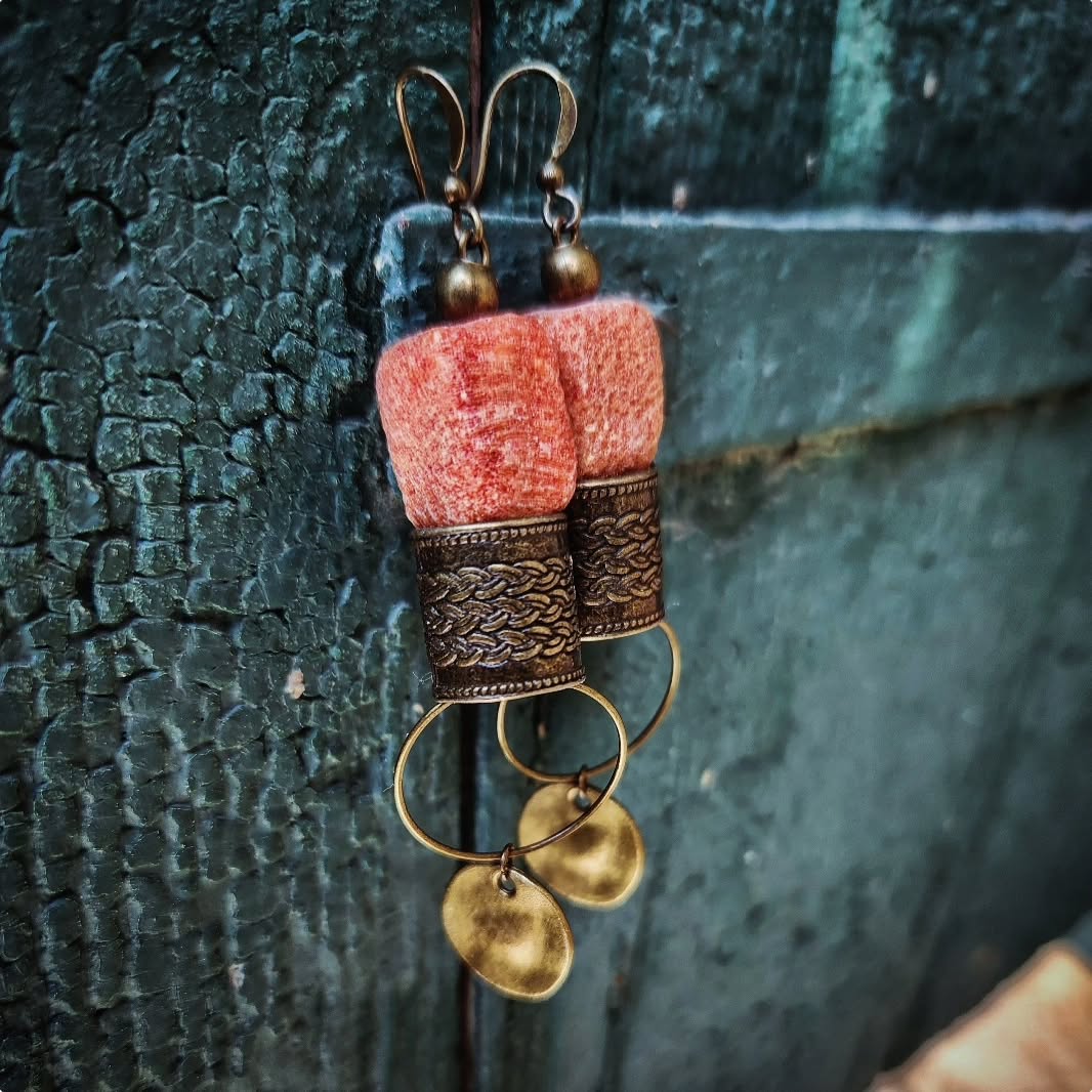 Bronze bohemian earrings with pink stone and gold accents on a textured dark background