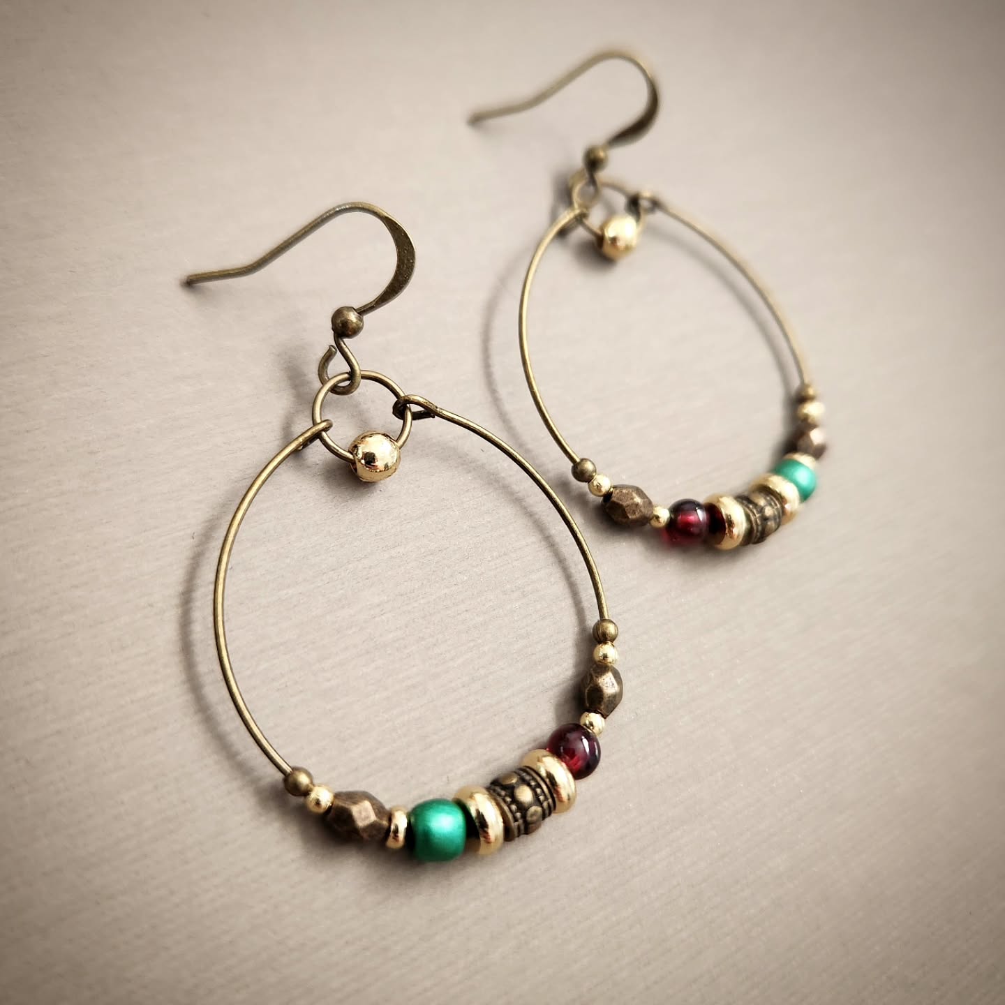 Bronze hoop earrings with colorful beads on a beige background