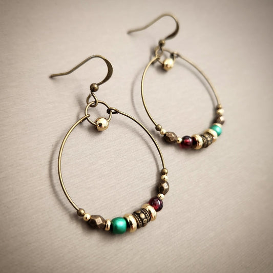 Bronze hoop earrings with colorful beads on a beige background