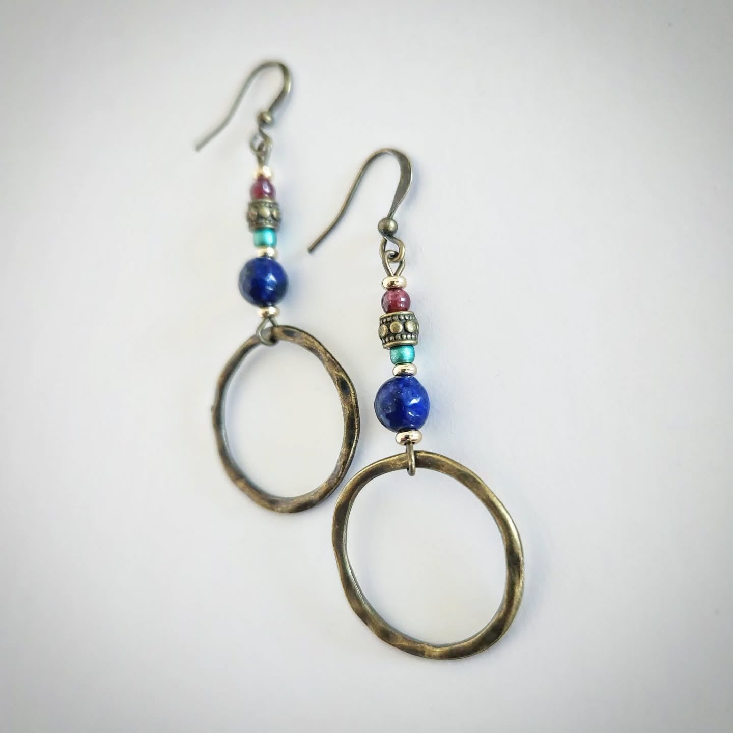 Pair of bronze earrings with colorful beads and a hoop at the end on a light gray background