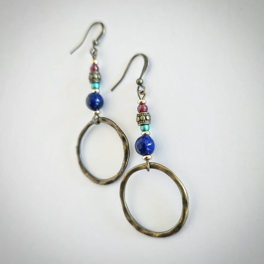 Pair of bronze earrings with colorful beads and a hoop at the end on a light gray background