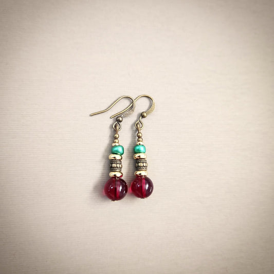 Pair of earrings with red, gold and turquoise beads on a beige background