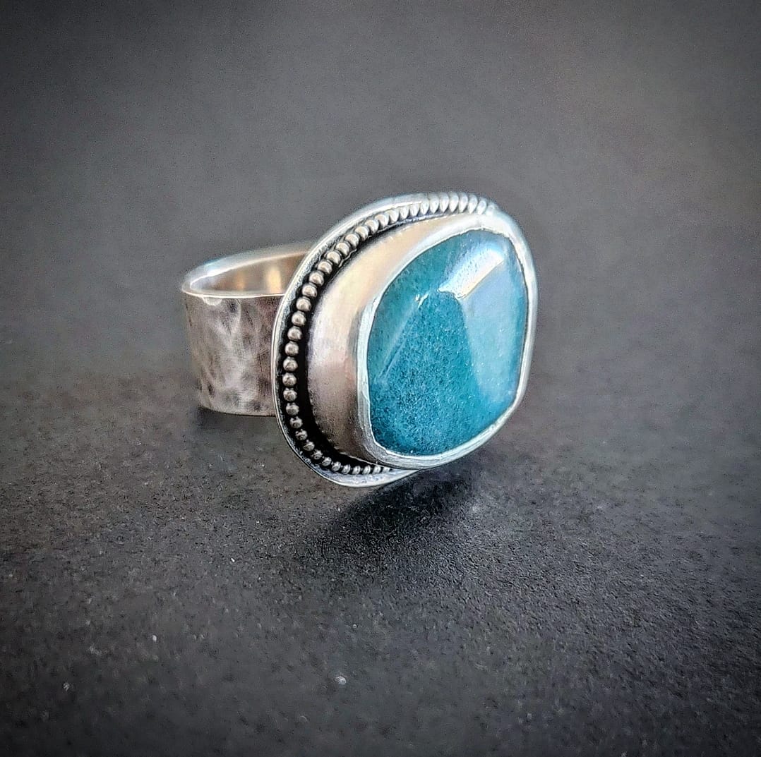 A silver ring with a large blue stone set in the center, surrounded by a dotted pattern on the metal