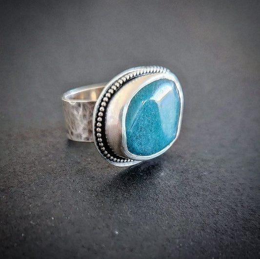 A silver ring with a large blue stone set in the center, surrounded by a dotted pattern on the metal
