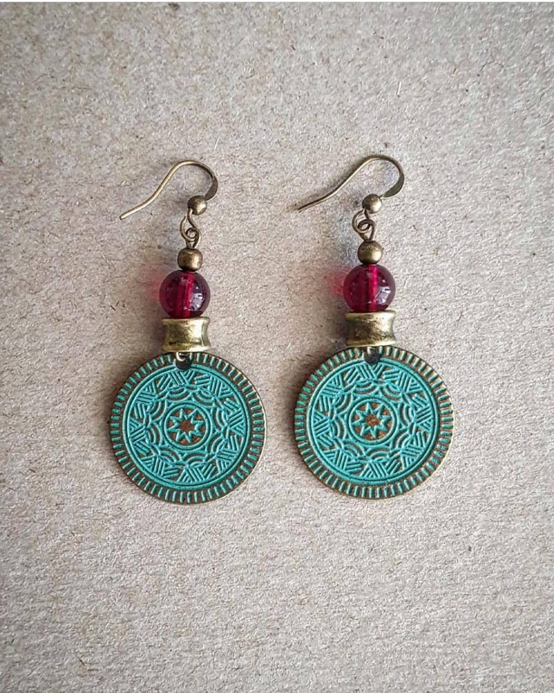 A pair of bronze coin earrings with intricate designs and red beads attached to them.