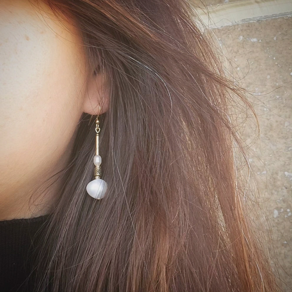 Close-up of an earring with a pearl worn by a person with brown hair.