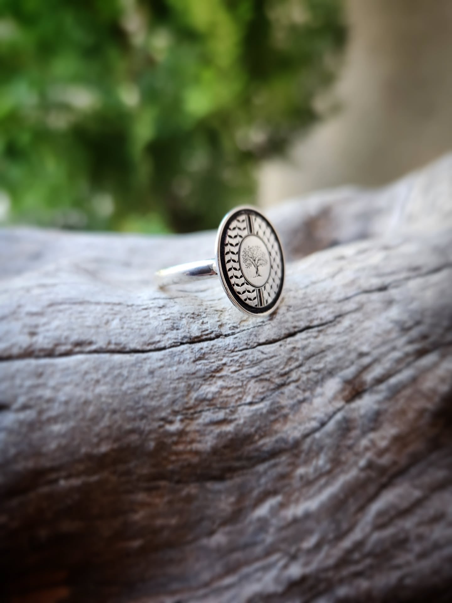 Silver ring with a circular tree design on a wooden surface with a blurred natural background